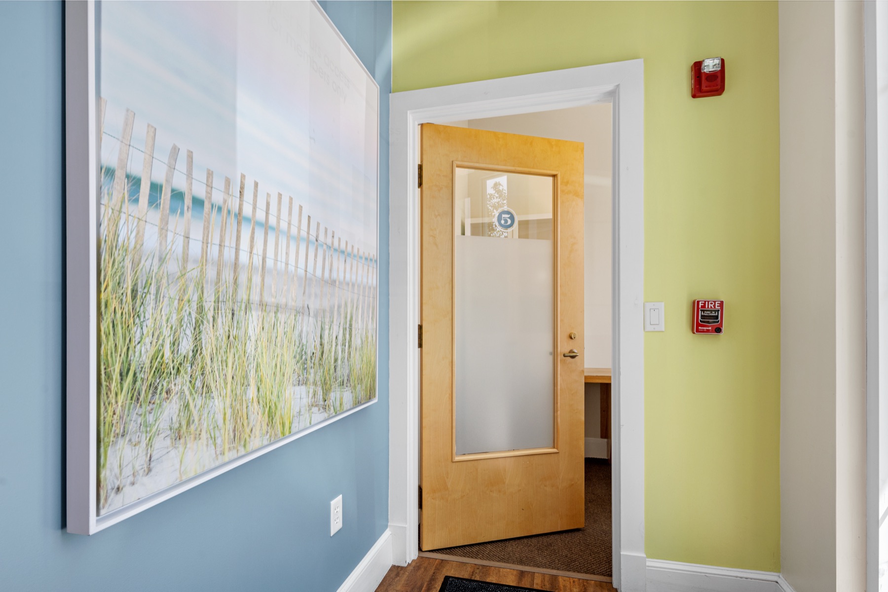 A hallway with beach artwork leading to a private office at Workspace Cohasset